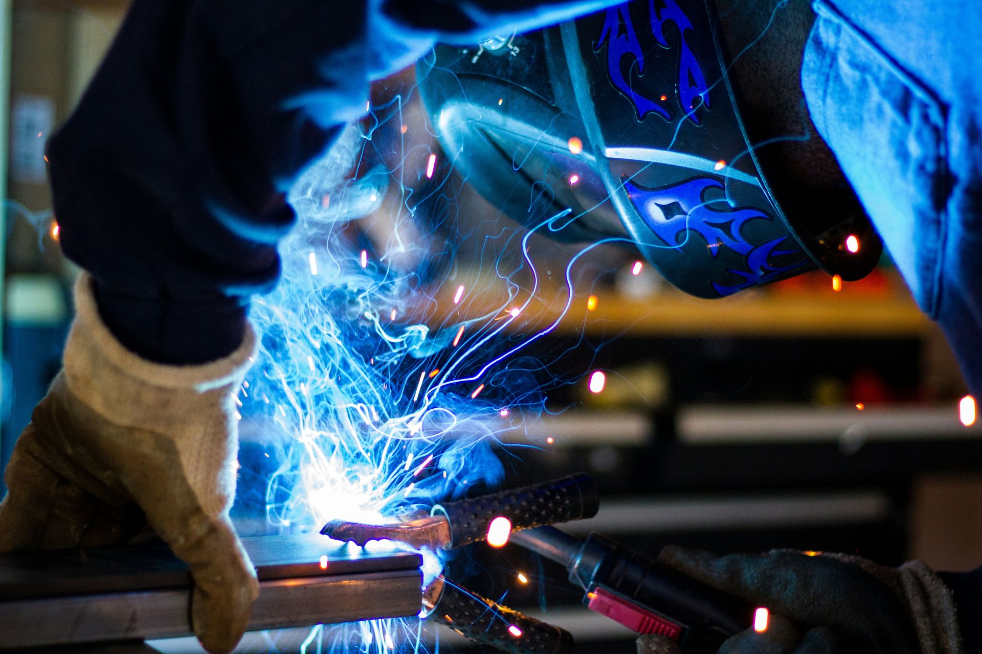 A welder wearing a protective helmet and gloves working on metal with sparks